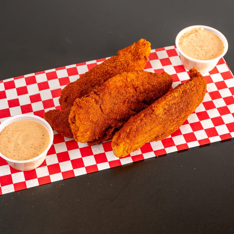 Crispy fried chicken tenders and wings served with two cups of creamy dipping sauce on red-and-white checkered paper.