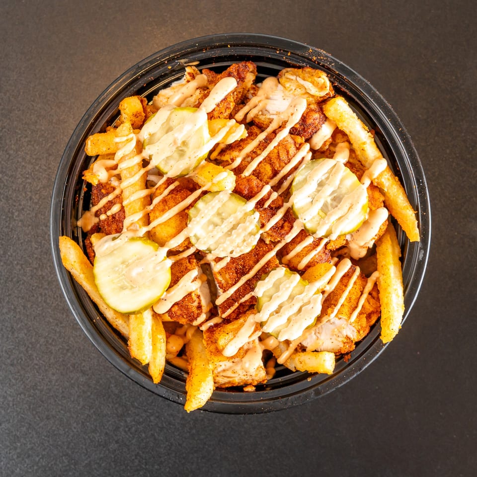 Loaded bowl of seasoned fries topped with crispy chicken, sliced pickles, and creamy sauce.