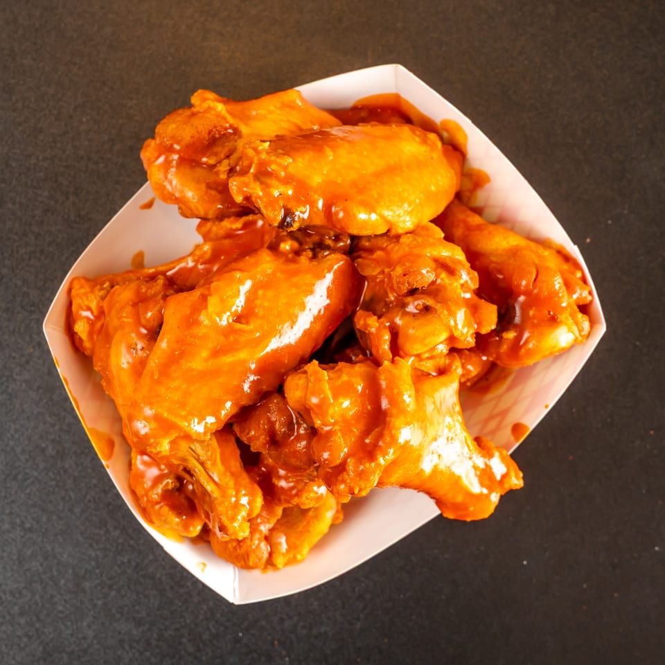 Basket of crispy chicken wings coated in glossy orange-red sauce on a dark tabletop.
