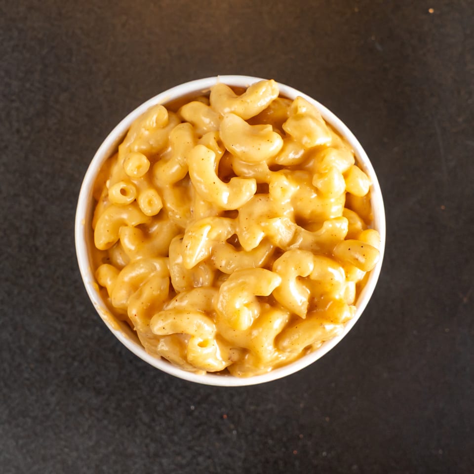 Overhead view of creamy cheese-coated elbow macaroni in a white bowl on a dark countertop.