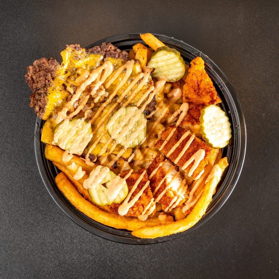 Loaded platter of seasoned fries topped with cheeseburger pieces, crispy chicken, pickles, and creamy sauce.