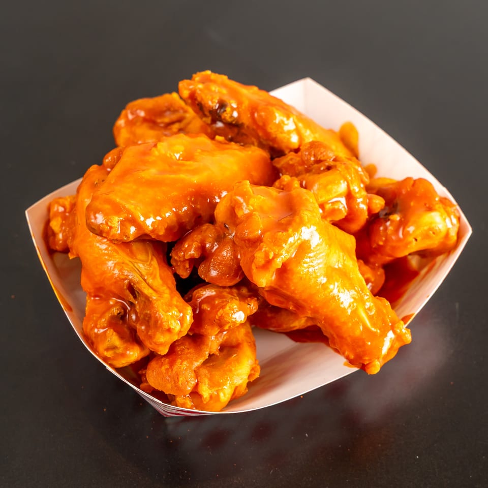 Basket of crispy chicken wings coated in glossy orange sauce on a dark tabletop.