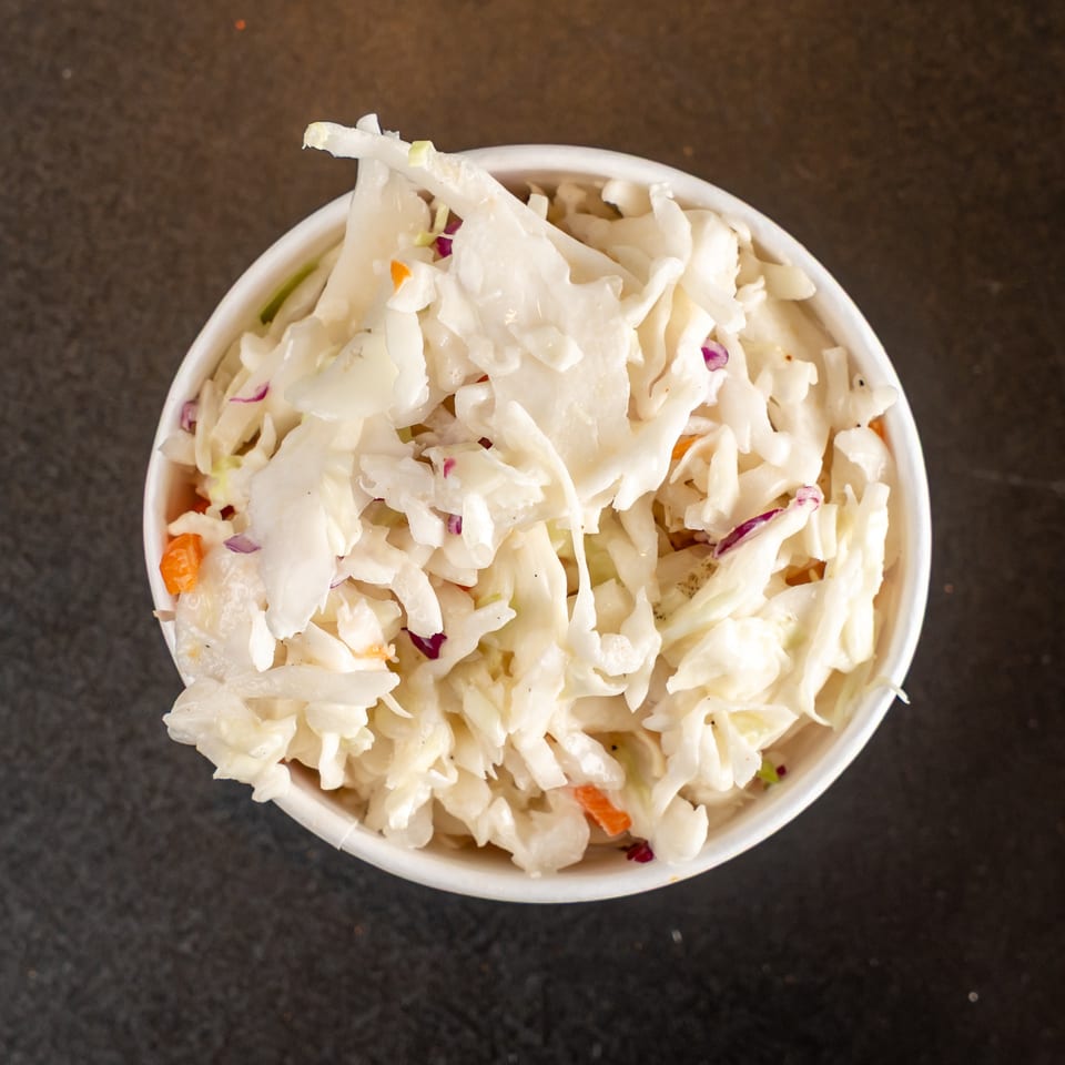 Overhead view of creamy coleslaw with shredded cabbage, carrots, and purple cabbage in a white bowl.
