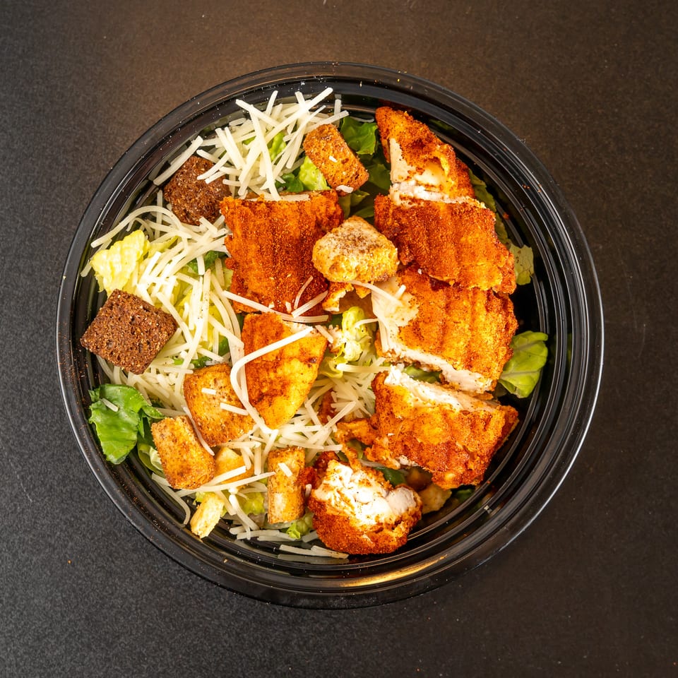 Overhead view of a salad bowl with lettuce, shredded cheese, croutons, and crispy breaded chicken pieces.